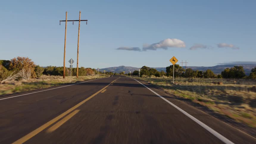 A first-person perspective driving along a scenic highway through the desert landscape of the American Southwest on a sunny day