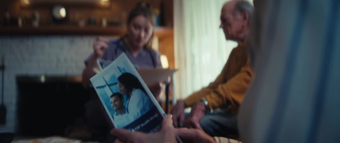 A home healthcare nurse explains a medical scan to an elderly man while his wife reviews a healthcare brochure