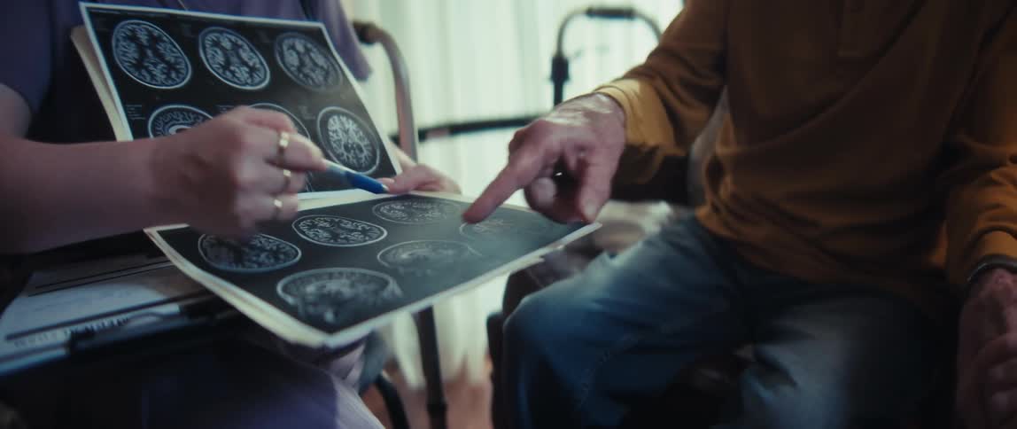 A nurse explains a brain scan to a concerned elderly man, who appears distressed by the diagnosis, in his home