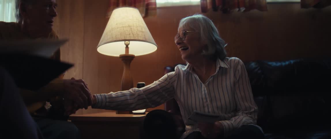 A senior woman's face lights up with a joyful smile and laugh as she shakes hands with a professional, sealing a deal