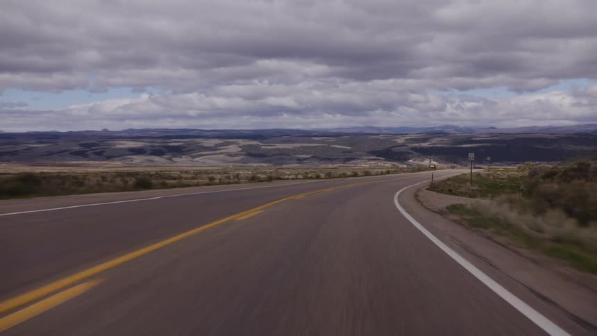 POV driving on a scenic highway through a vast landscape under a dramatic, cloudy sky