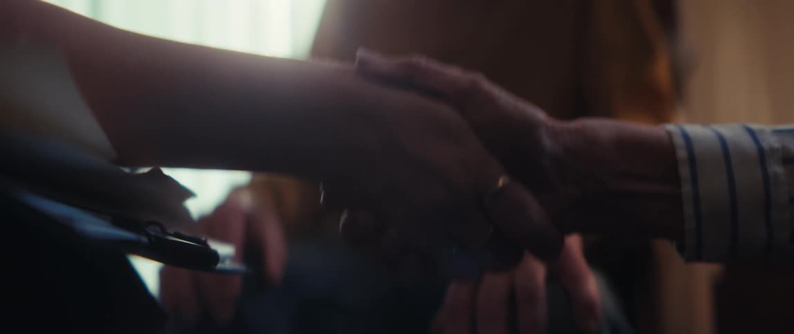 An elderly man laughs with delight as a younger person gently holds his hand in a tender moment