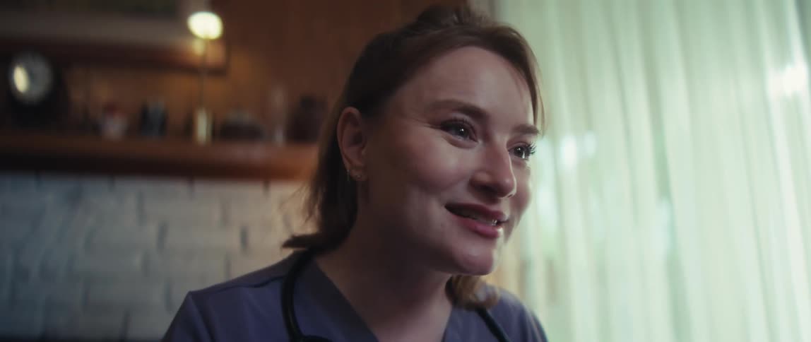 A close-up of a caring female nurse in scrubs talking and smiling kindly