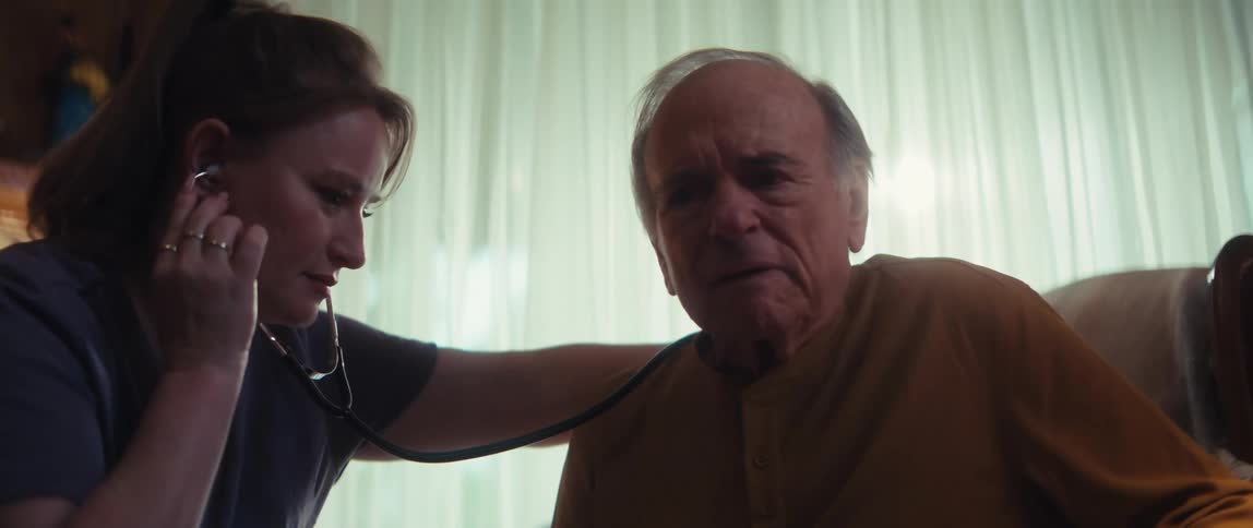 A compassionate home healthcare nurse carefully listens to an elderly man's chest with a stethoscope during an in-home check-up