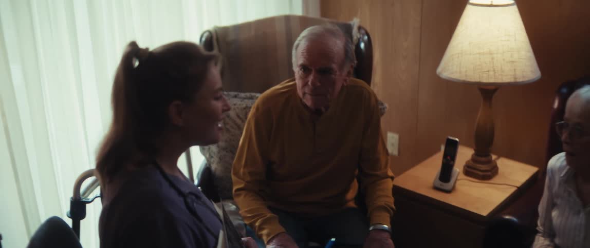 A home healthcare nurse delivers somber news while reviewing a brain scan with an elderly couple, who then hold hands for support