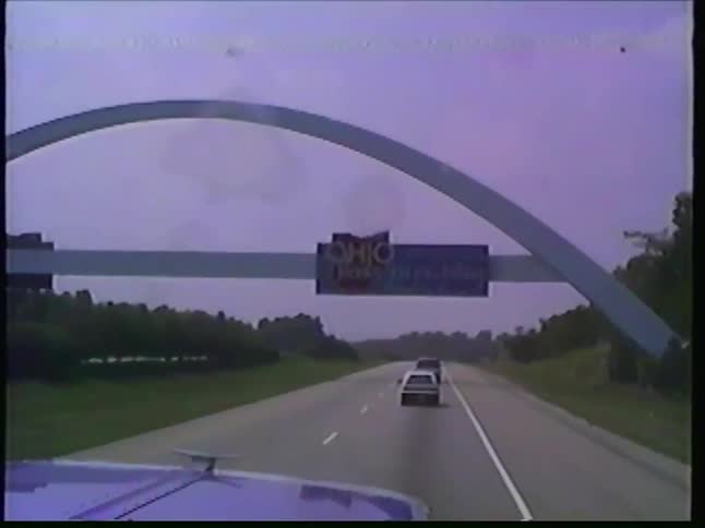 Archival dashcam footage shows a truck driving on a rural highway and passing under the 'Thank you for visiting Ohio' archway sign