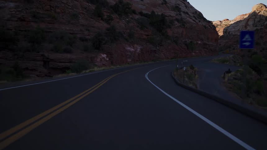 Driving on a scenic highway through a dramatic red rock canyon as evening light fades into shadow