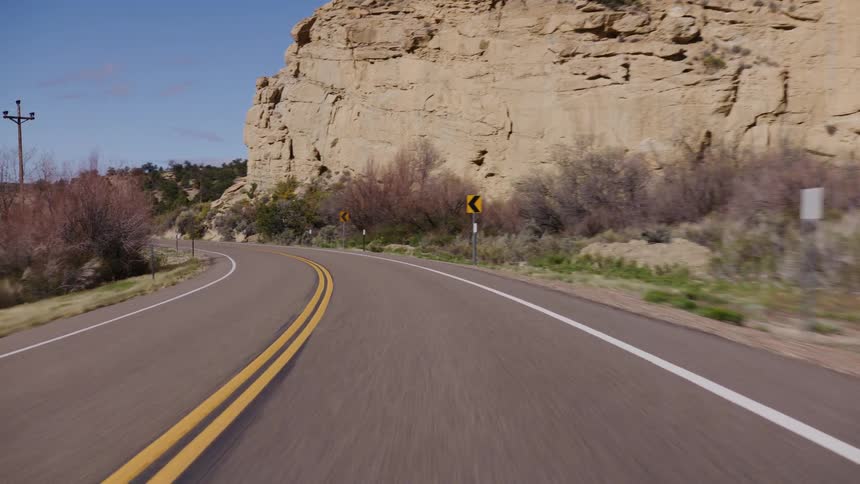 POV shot of a smooth drive on a winding desert highway that curves alongside a rocky canyon wall under a clear blue sky