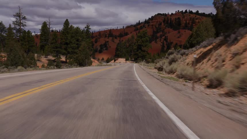 A scenic point-of-view drive on a winding highway through the red rock hills and pine forests of a national park