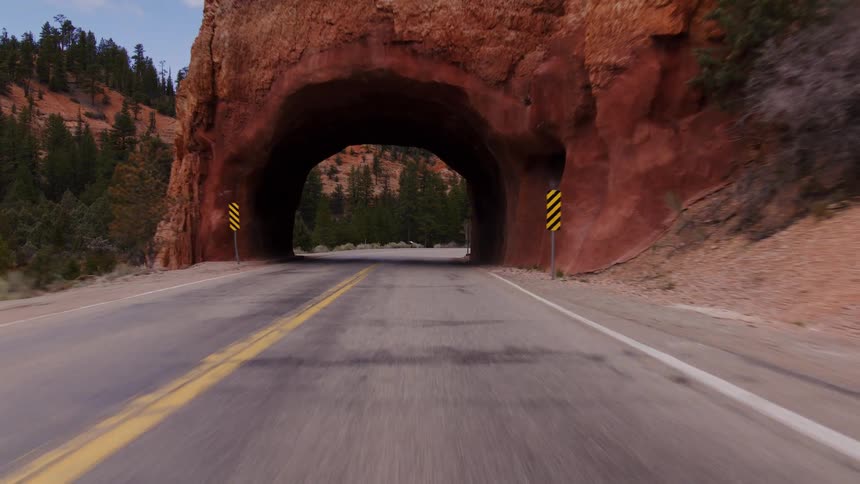 A point-of-view shot driving on a scenic highway through a tunnel carved into the iconic red rocks of a canyon landscape