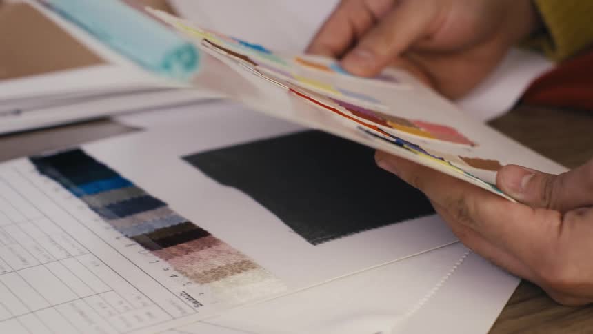 Close up of a designer's hands selecting colorful fabric swatches from a sample book for a new design project