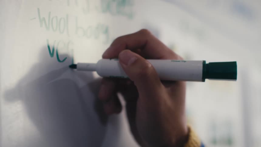 Close-up shot of a hand writing the word vegan on a whiteboard with a green marker in slow motion