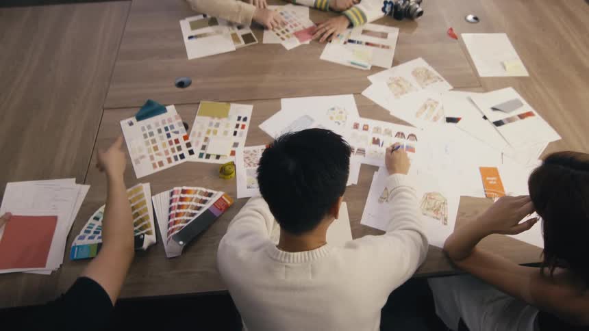 A camera booms up to an overhead view of a team of fashion designers collaborating on a new clothing collection in their creative studio