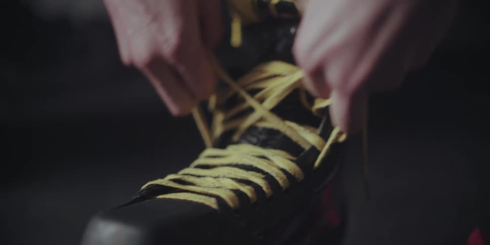 A hockey player carefully ties the yellow laces on their ice skate in slow motion