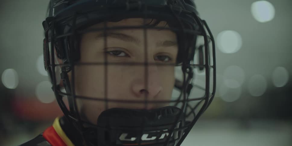 A close-up of a young hockey player's intense and determined eyes looking through their helmet cage