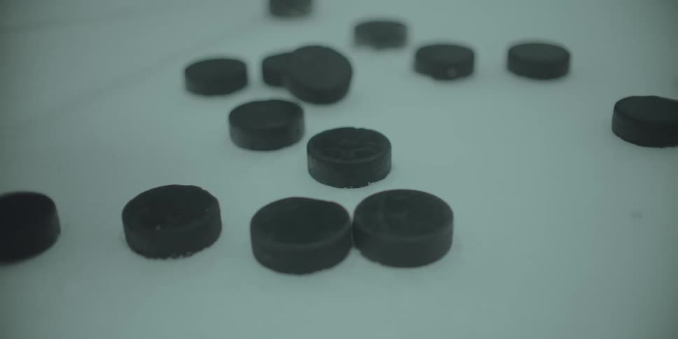 A close-up of a hockey stick on the ice rink tapping multiple hockey pucks in slow motion