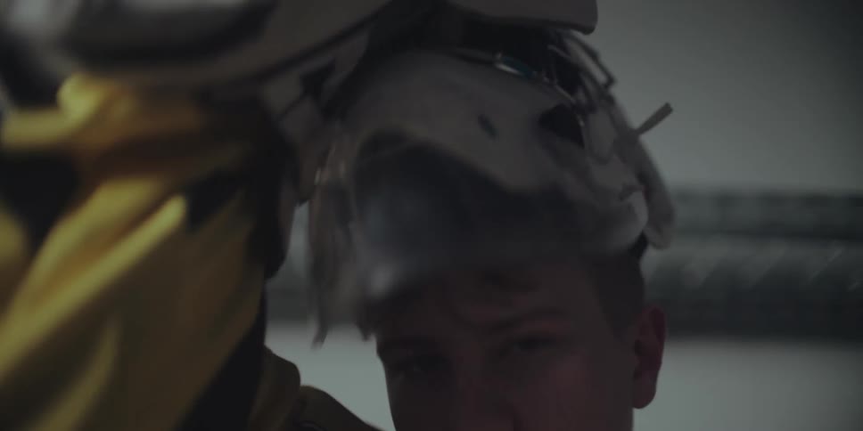 A focused young ice hockey goalie slowly puts on his helmet and glove in a dimly lit locker room before a game
