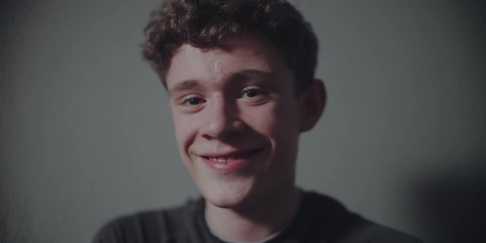 A close-up portrait of a happy teenage boy with curly hair smiling genuinely at the camera