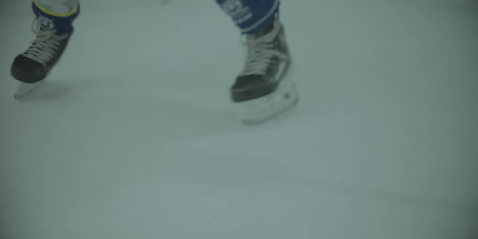 An ice hockey player hits a puck with their stick on the rink in a slow-motion close-up