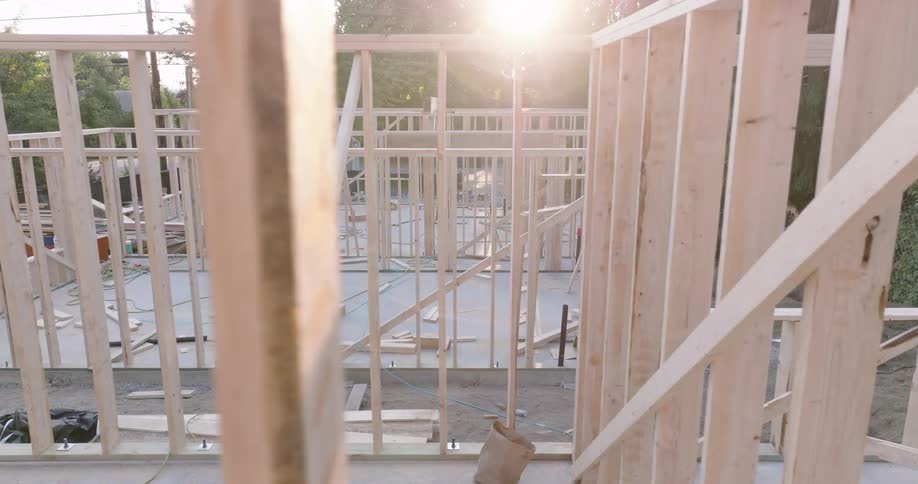 Sunshine flares between studs of the wooden framing of new homes under construction
