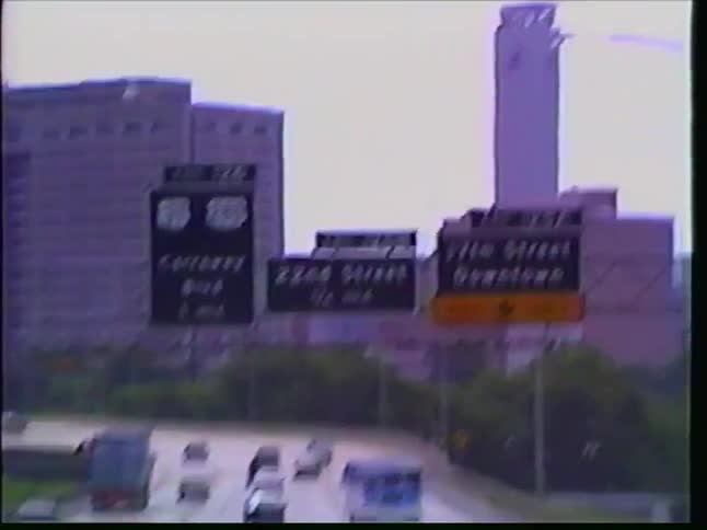 Retro VHS footage captures a point-of-view drive along a busy highway heading towards a city skyline