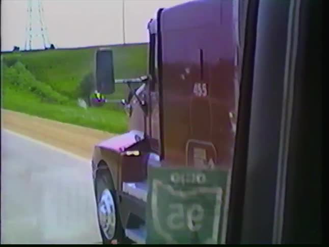 Vintage VHS footage from a moving vehicle captures a semi-truck driving alongside on a rural highway