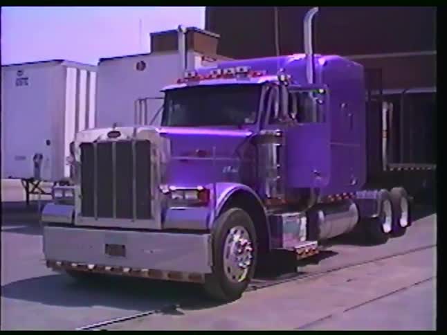 A slow zoom shot showcases a vibrant custom purple Peterbilt semi-truck parked in an industrial loading dock area