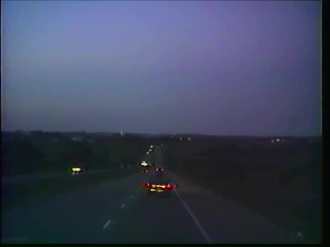 A point-of-view shot from a truck driving on a dark highway at twilight, with the taillights of other cars visible ahead