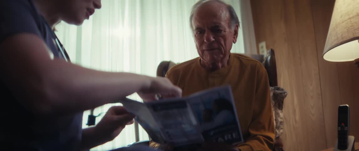 A caring home health nurse consults with an elderly couple in their living room, explaining the benefits of their services from a brochure