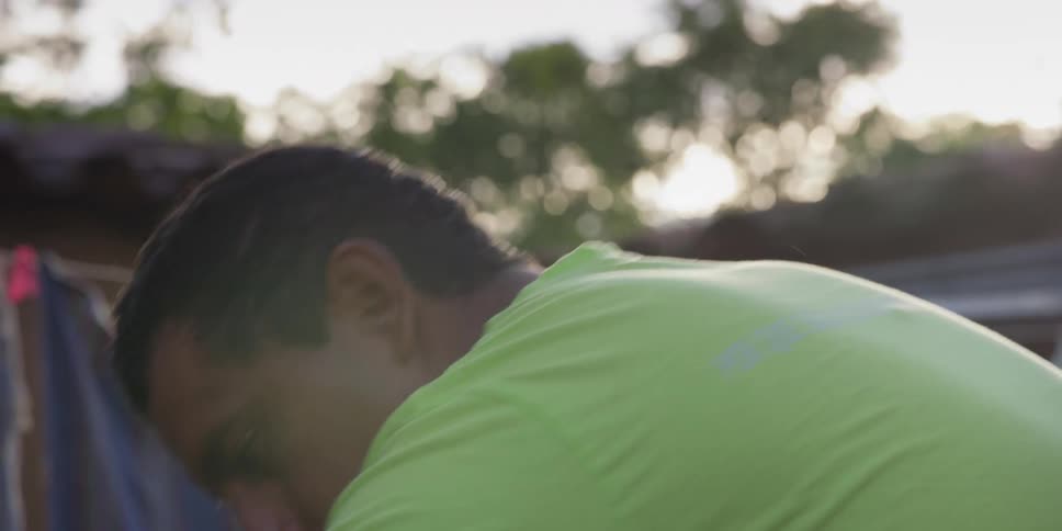 A hardworking man in a green t-shirt diligently focuses on his task outdoors in slow motion