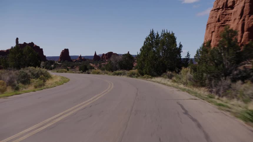 A smooth POV shot driving down a winding road alongside towering red rock formations in a desert landscape