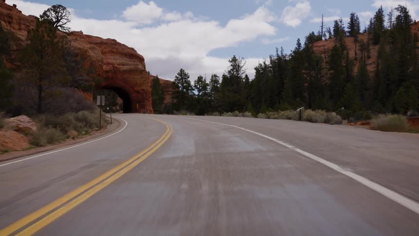 A scenic point-of-view shot reversing on a winding highway away from a unique red rock tunnel