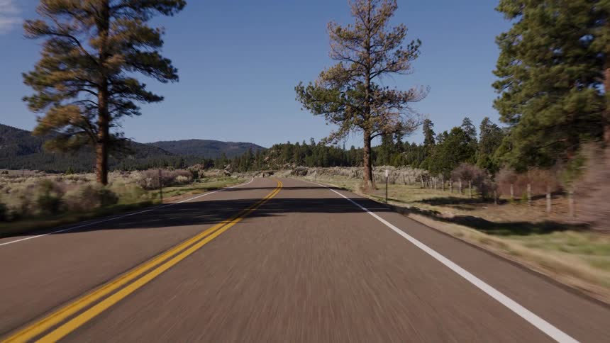 A scenic POV drive along a winding two-lane highway through a hilly, forested landscape on a sunny day