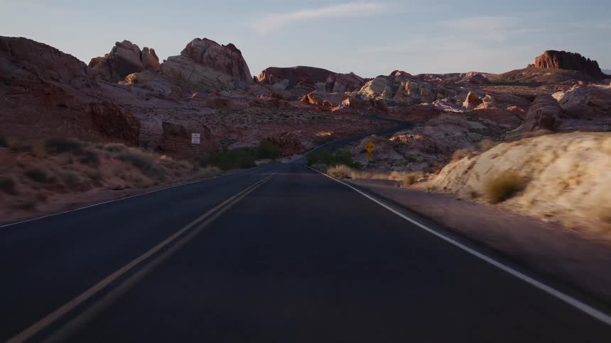 A slow-motion point-of-view drive along a winding road through the Valley of Fire State Park in Nevada during a beautiful golden hour sunset