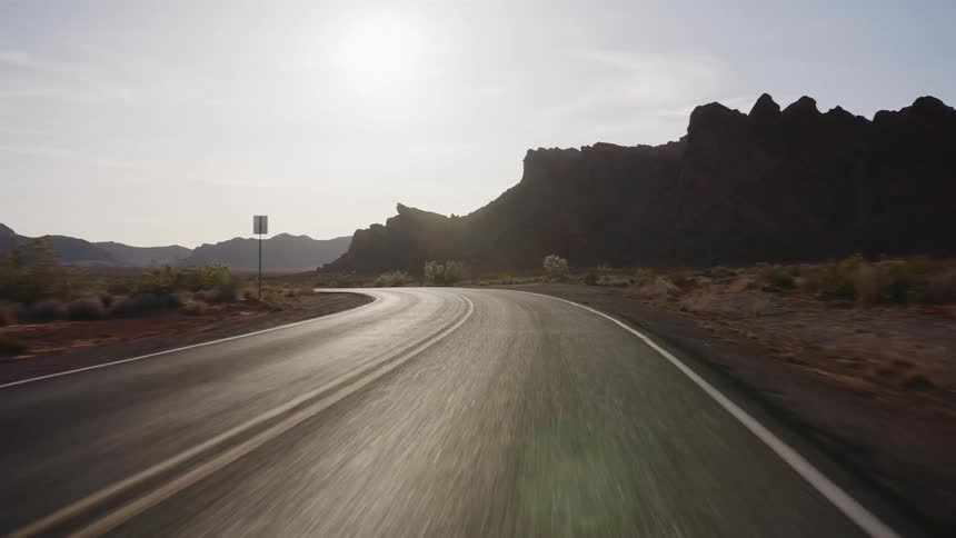 A smooth point-of-view shot driving down a winding highway through a desert canyon at sunrise