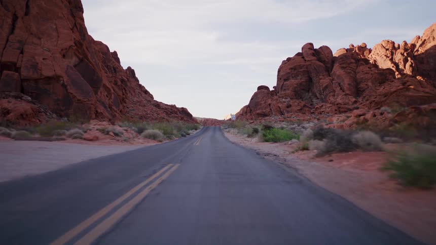 A smooth point-of-view drive down an empty desert road nestled between stunning red rock formations