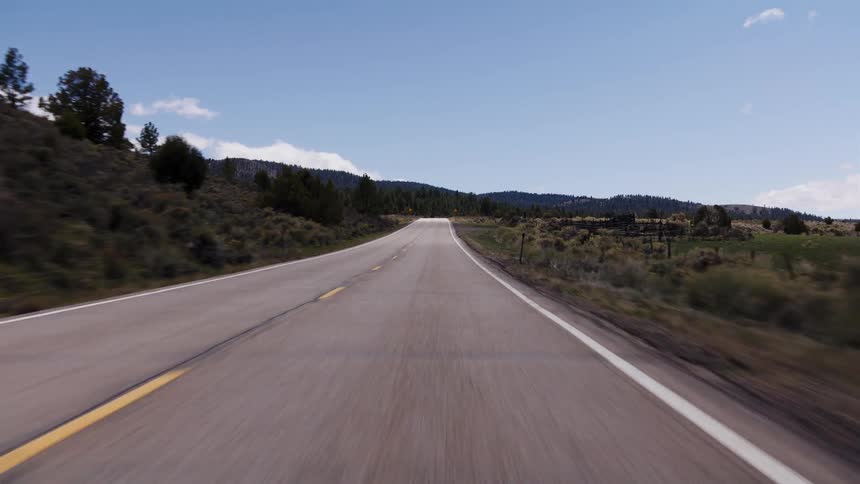 Point-of-view shot driving down a winding two-lane road through a scenic mountain landscape on a sunny day