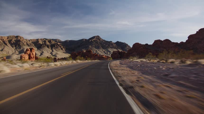 A cinematic point-of-view drive along an empty desert highway surrounded by dramatic red rock formations and mountains