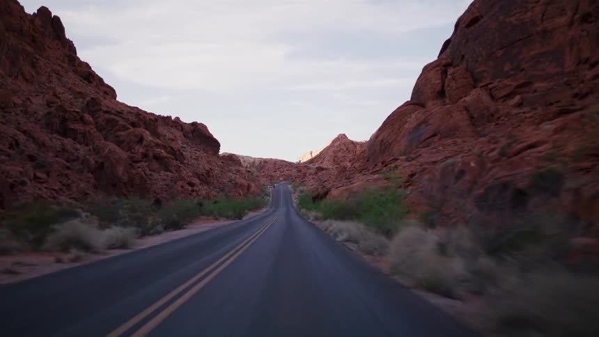A slow, scenic drive on an empty road winding through a majestic red rock canyon at dawn