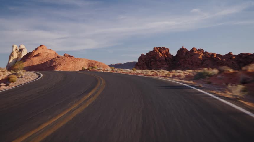 A point-of-view driving shot along a winding desert road through the vibrant red rock formations of the Valley of Fire at sunrise