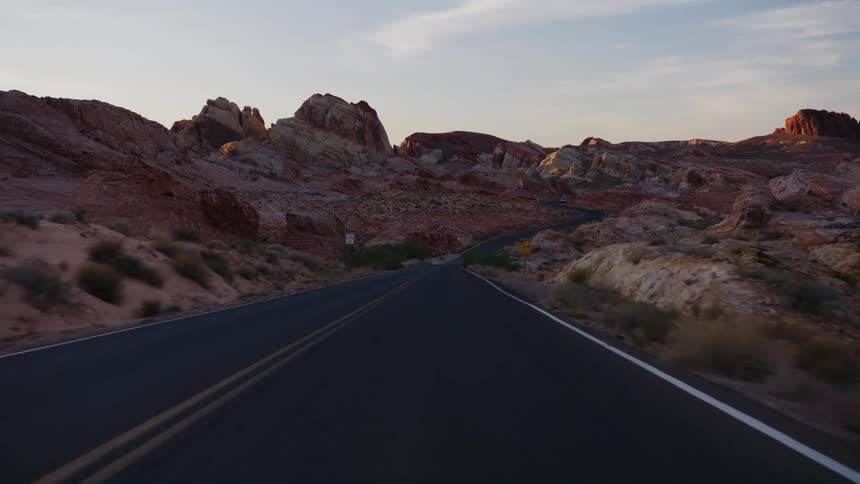 A scenic point-of-view drive on a winding road through a colorful desert canyon landscape at sunrise