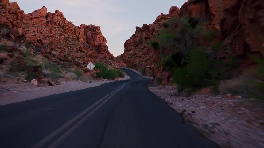 A slow, point-of-view drive along a winding, paved road through a dramatic red rock canyon at dusk