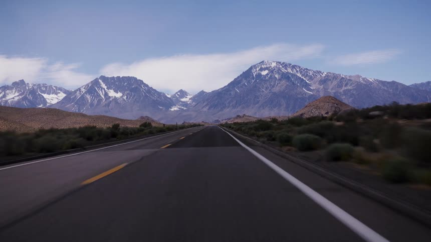A point-of-view shot captures the feeling of driving down a scenic desert highway toward a majestic, snow-capped mountain range