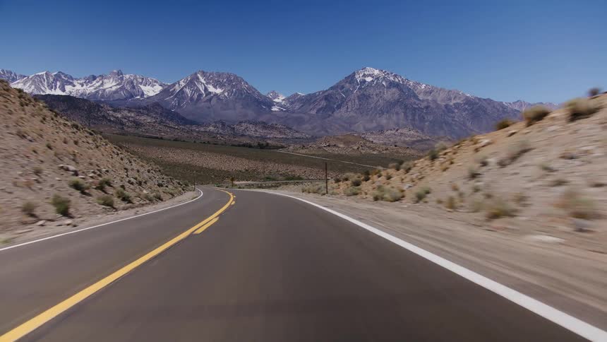 A scenic drive on a winding desert highway reveals a stunning view of snow-capped mountains in the distance