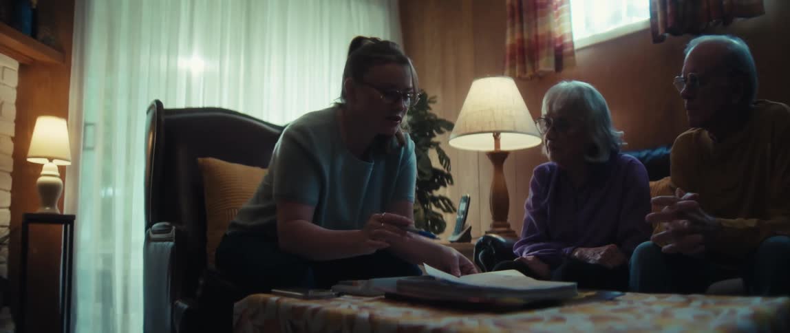 A young advisor meets with a senior couple in their living room to carefully review and explain important documents