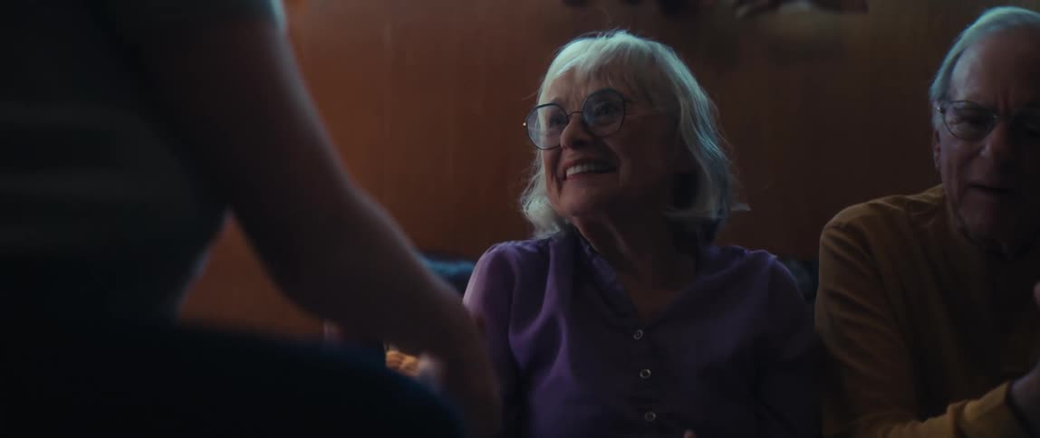 A joyful elderly woman with glasses laughs as she plays a hand-clapping game with her grandchild in a warmly lit room