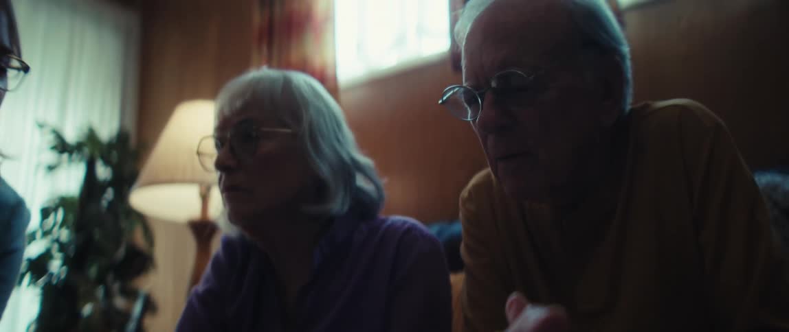 A financial advisor carefully reviews a performance report with a concerned elderly couple in their living room