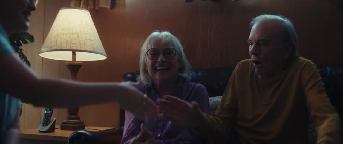 An overjoyed elderly couple celebrates good financial news with their advisor, shaking hands and hugging happily in their living room