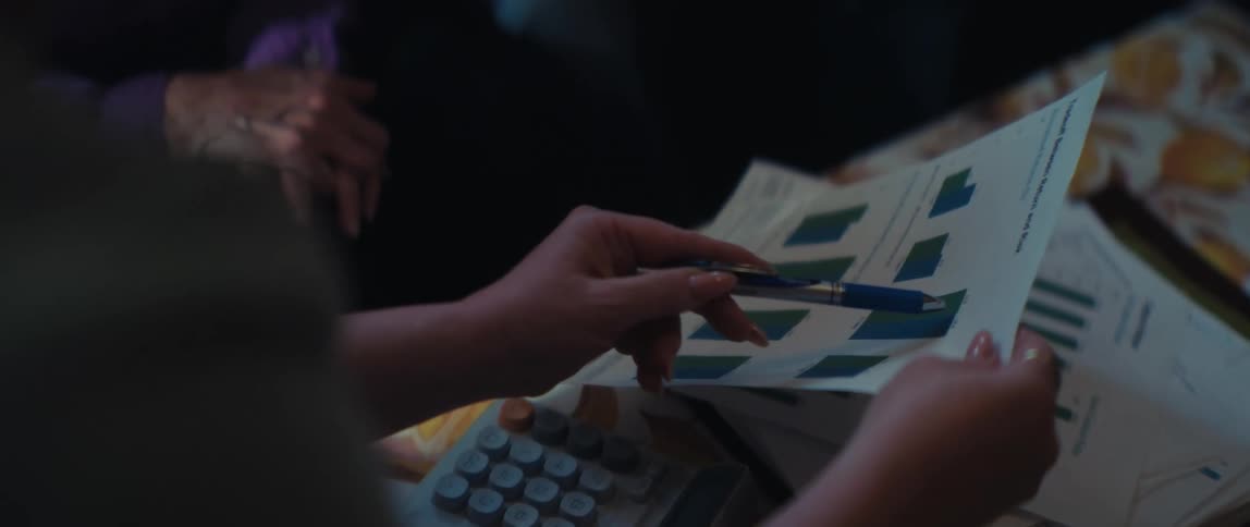 A business professional's hands point with a pen at bar charts on a printed report while analyzing data