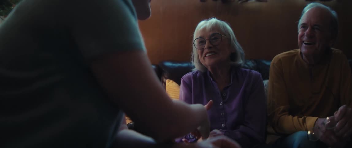 A financial advisor explains paperwork to a happy senior couple, who then shake hands in agreement in their cozy living room